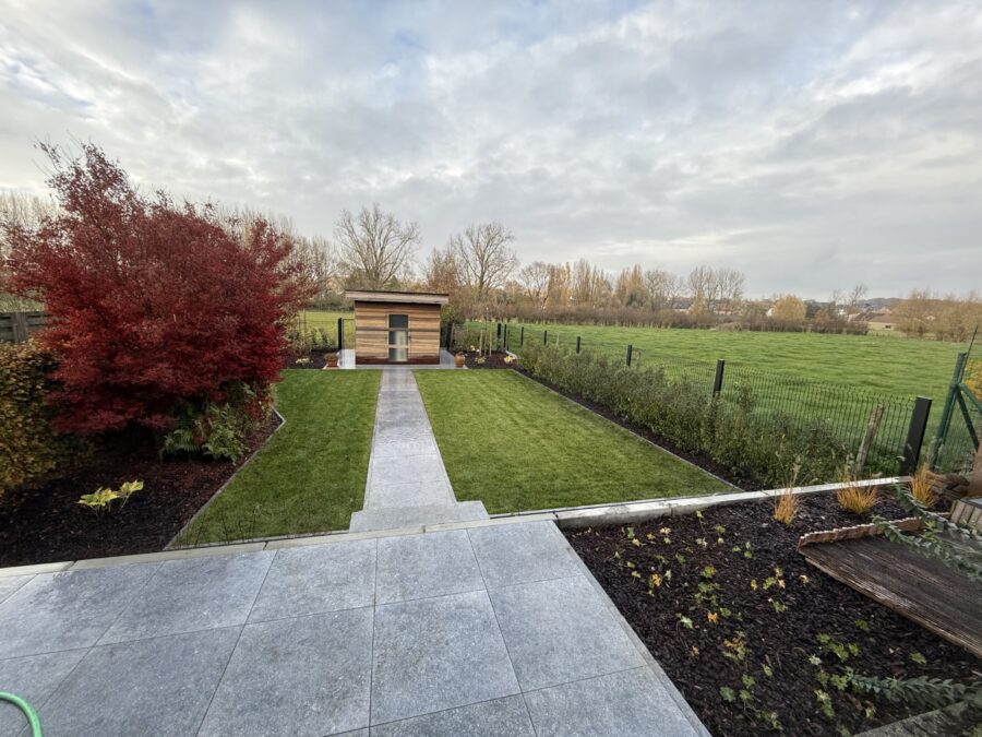 Strak aangelegd groen gazon met tuinpad en tuinhuis